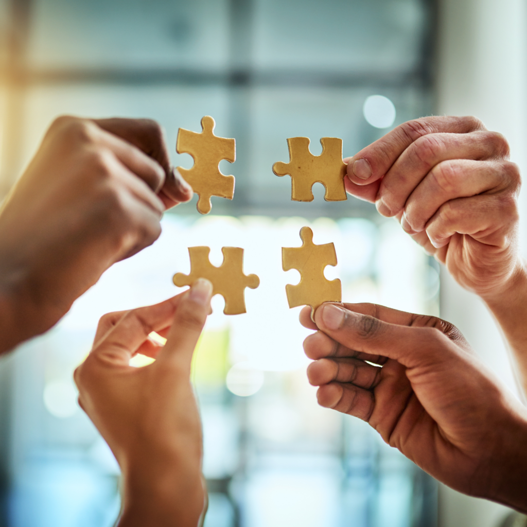 four hands holding up connecting puzzle pieces